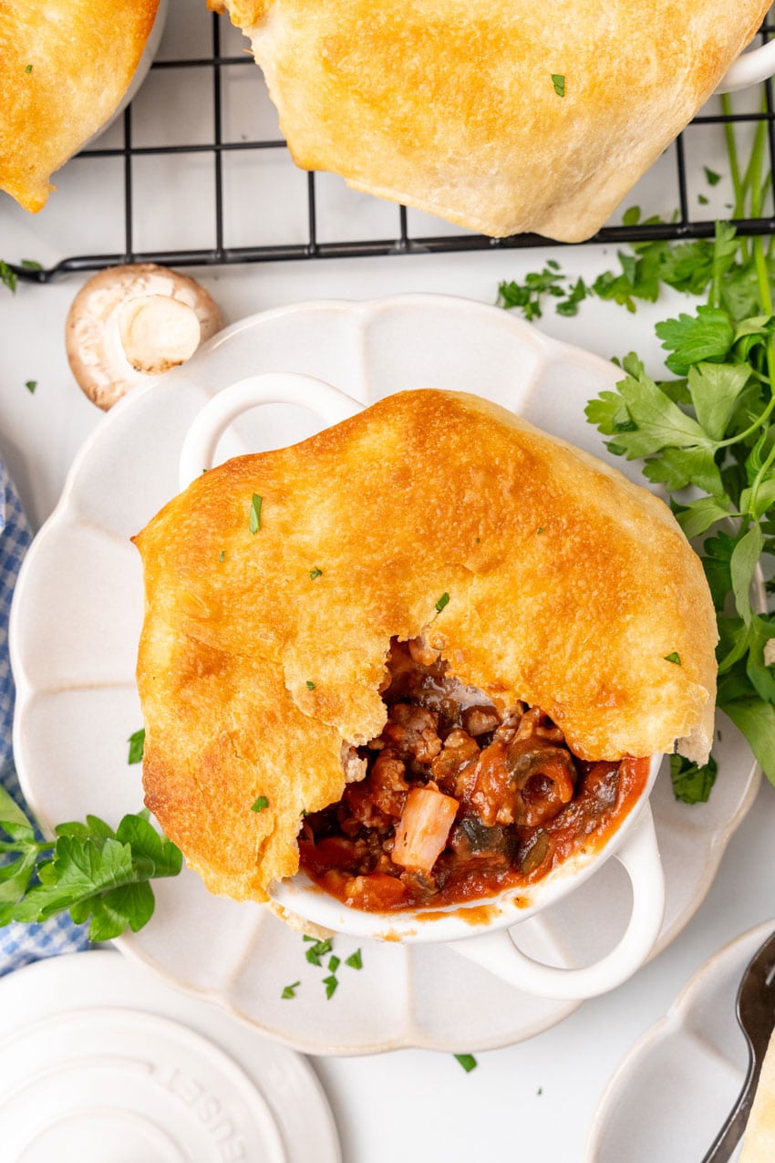 pizza pot pie in a white ramekin on a small white scalloped plate surrounded by fresh herbs