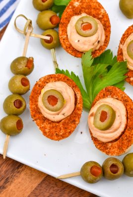 bloody mary deviled eggs arranged on a white platter with fresh parsley leaves and olives on toothpicks