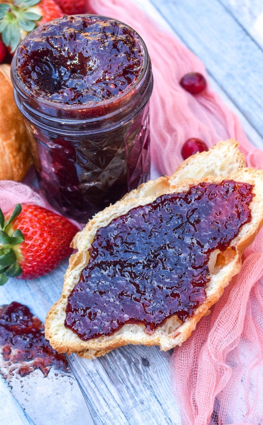 homemade christmas jam spread over half a croissant roll surrounded by fresh strawberries and cranberries