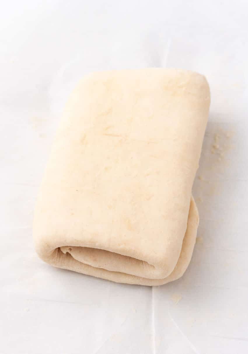 a tri folded sheet of homemade puff pastry resting on a piece of white parchment paper