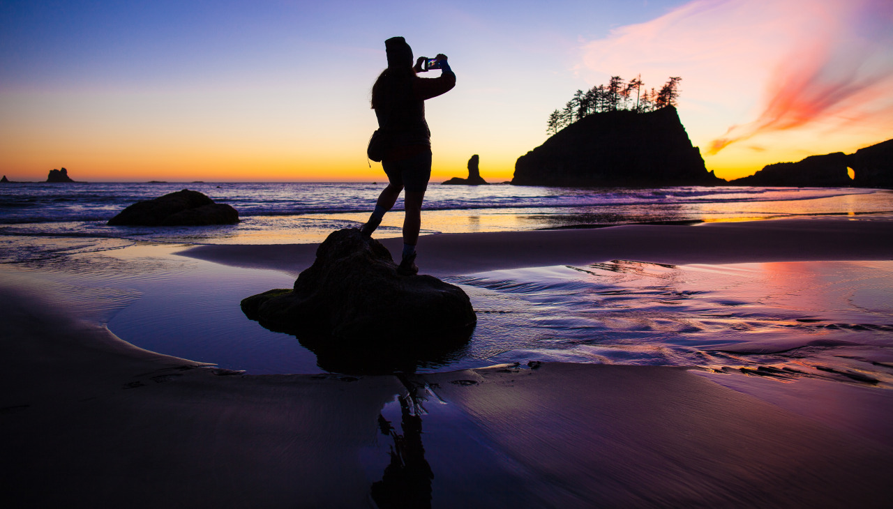 Woman standing on a rock, taking a photo of a beautiful sunset in Olympic Coast.