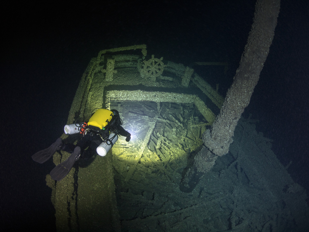 Diver examines a shipwreck in dark waters.