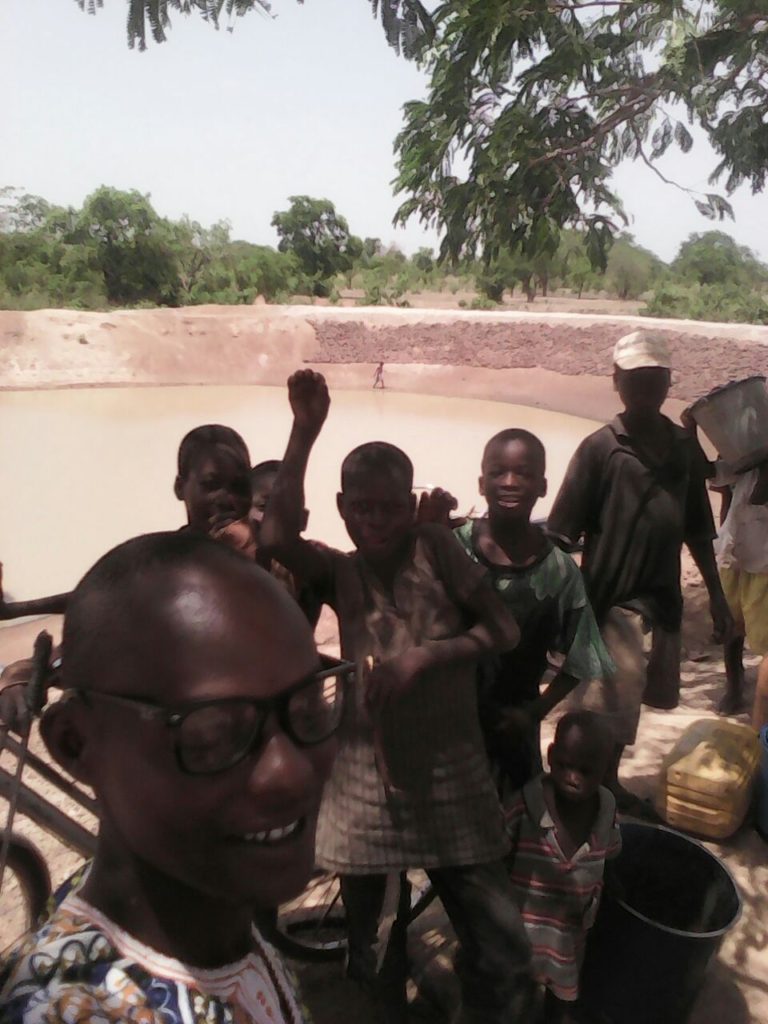 The community of Vogyili reinforces their dugout in the hope that it will hold more water this rainy season (background). In the foreground, kids pose with Eric