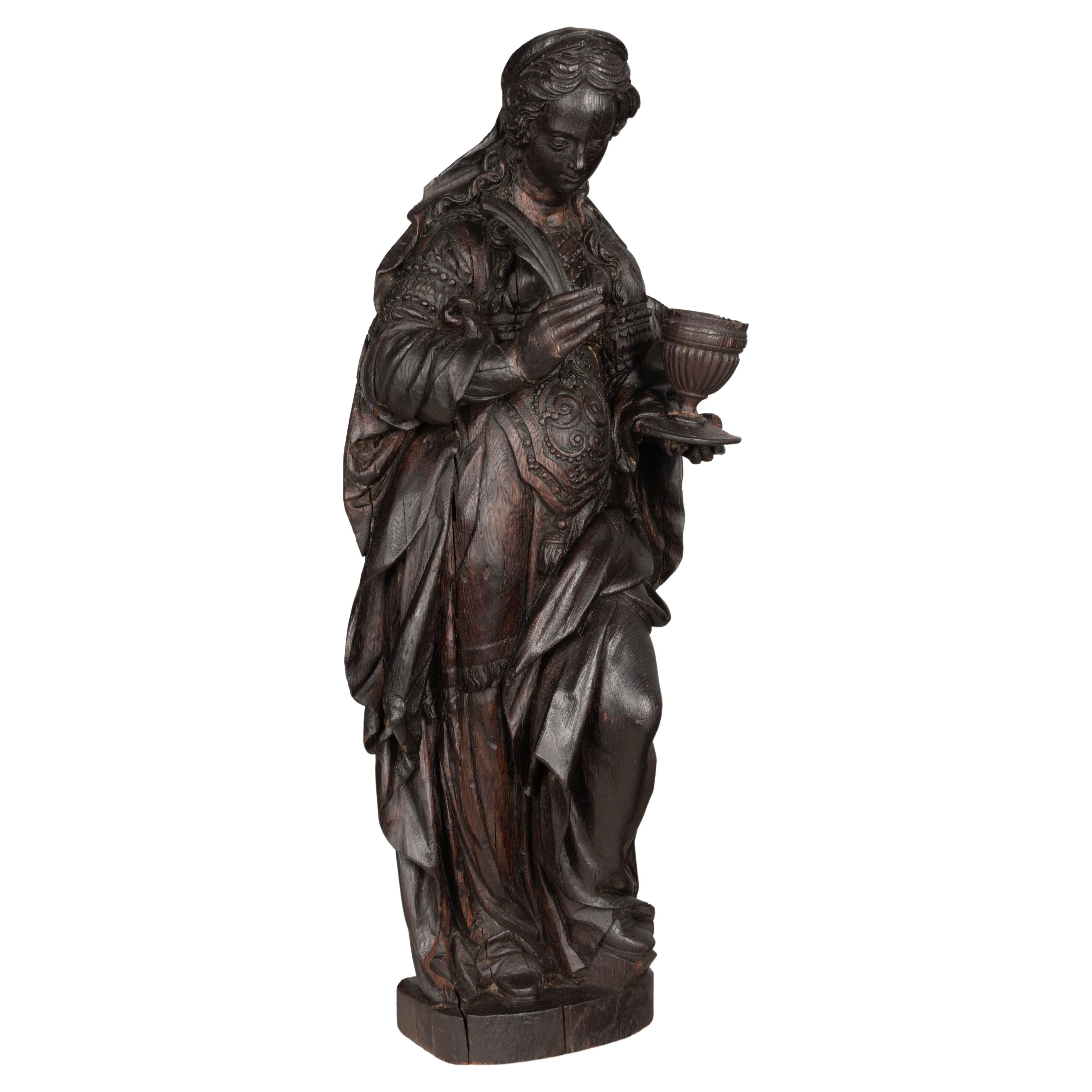 An 18th century Continental carved oak sculpture or wall hanging depicting St. Mary Magdalene holding a sacred chalice. Beautifully detailed draped gown. Dark stain with waxed patina. Wire on the back to display on a wall. Some splits in wood, minor