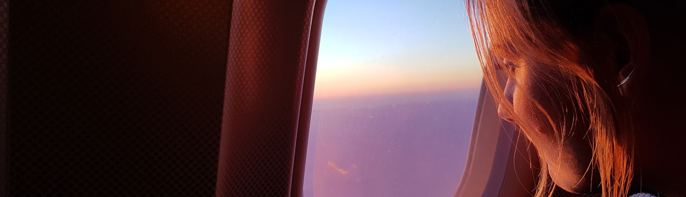 A woman on a plane, looking out the window at sunset.