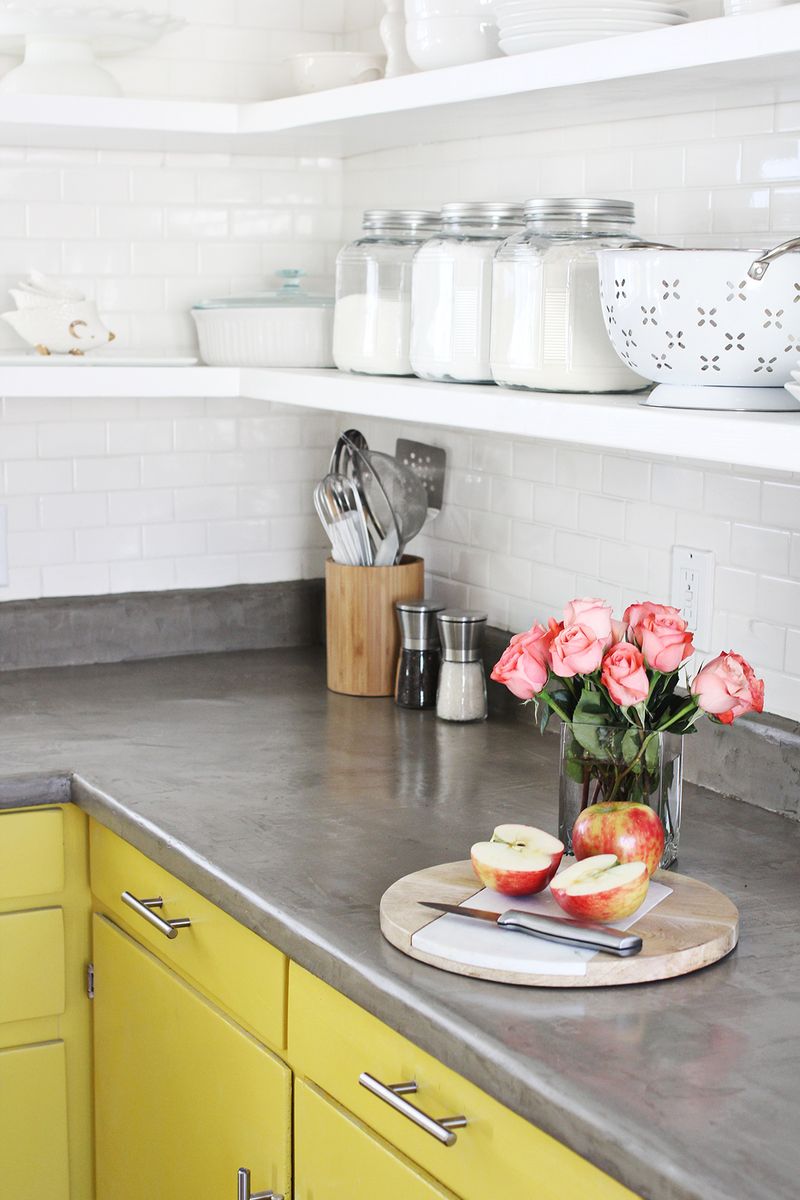 a kitchen with yellow cabinets, white brick walls, and concert countertops with a sliced apple on top