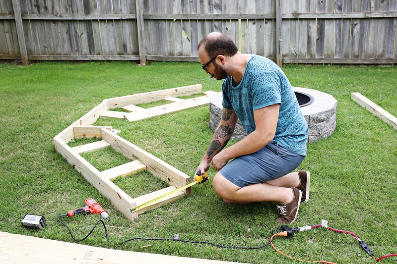 a man measuring the bottom of the bench with power tools around him