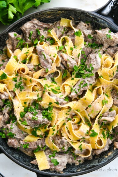 Photograph of beef stroganoff in a skillet with egg noodles and topped with parsley.