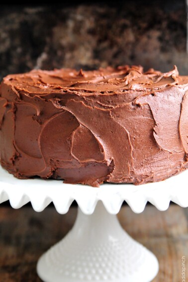 Chocolate Cake with Chocolate Buttercream Frosting on a white cake plate and dark background.