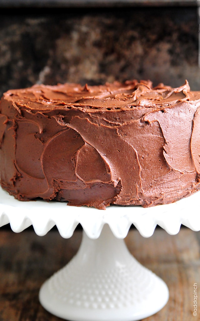 Chocolate Cake with Chocolate Buttercream Frosting on a white cake plate and dark background.