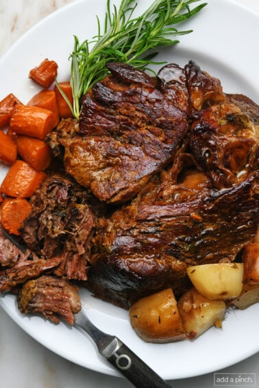 Photo of pot roast with carrots and potatoes on white plate.