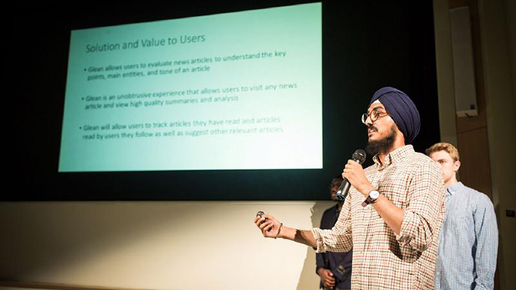 Two students stand in front of a crowd at a conference and present their research