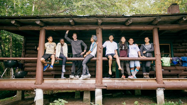 Several students sit on the porch of a Dartmouth Outing Club cabin