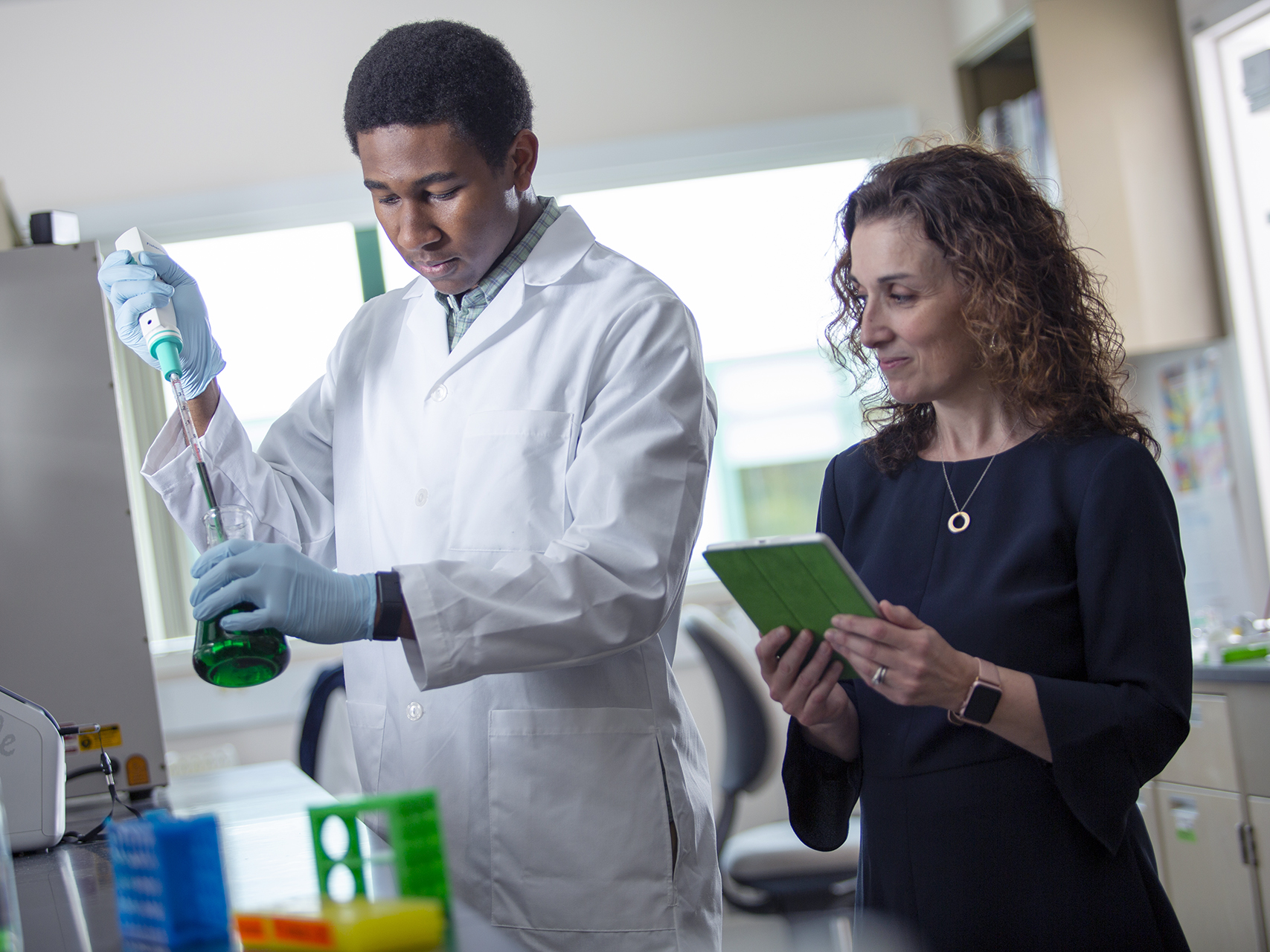 two people in a lab adding liquid to a beaker