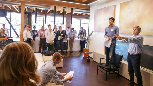 A group of people standing around as a speaker giving a presentation points to a member of the audience.