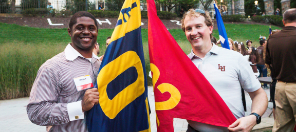 Two alumni standing with the flags that represent their class years.