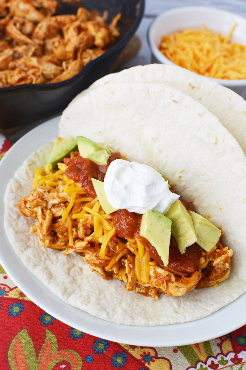 A plate of shredded chicken tacos with ranch and toppings.