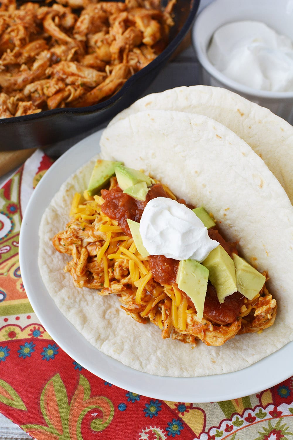 Overhead shot of chicken ranch tacos on a plate with shredded chicken in the background. 