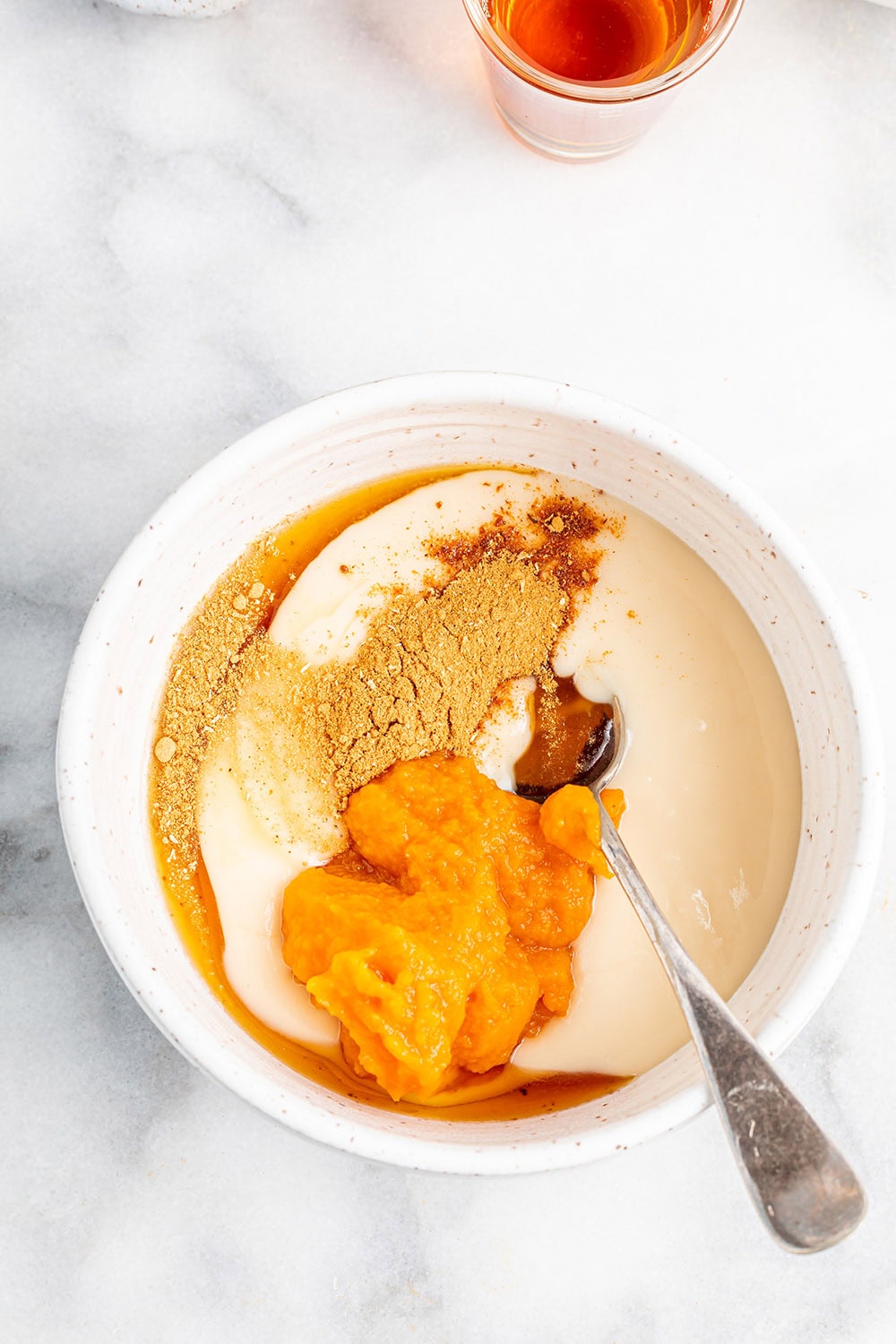 Pumpkin puree, pumpkin pie spice, and coconut butter being mixed in a bowl. 