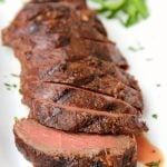 grilled venison backstrap sliced on a platter with fresh herbs