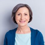 Portrait of attractive cheerful middle-aged woman wearing blue cardigan isolated over grey color background