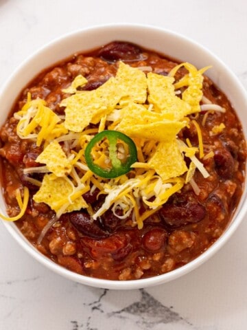 Bowl of crockpot chili topped with corn chips, shredded cheese, and jalapeno.