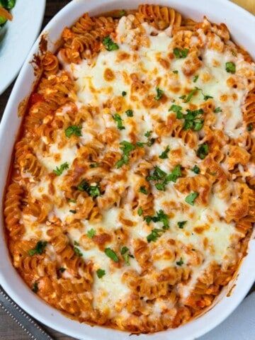 Cheesy Italian Baked Rotini in white casserole dish topped with fresh minced parsley next to tossed salad.