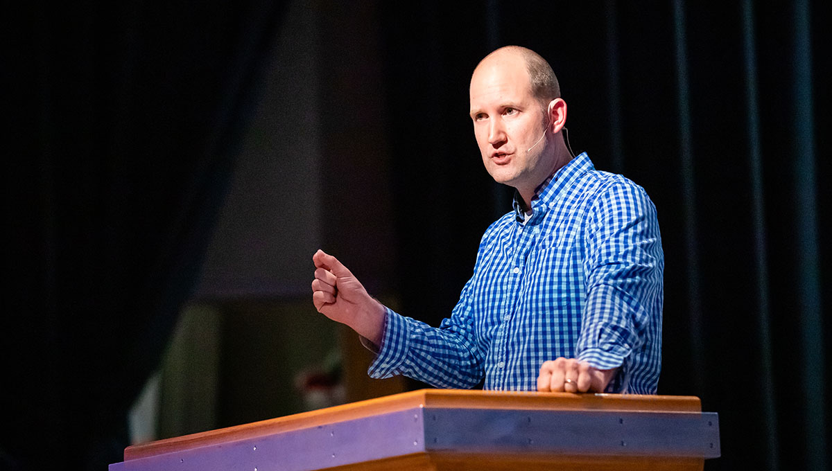 Man in blue button up shirt preaching on stage