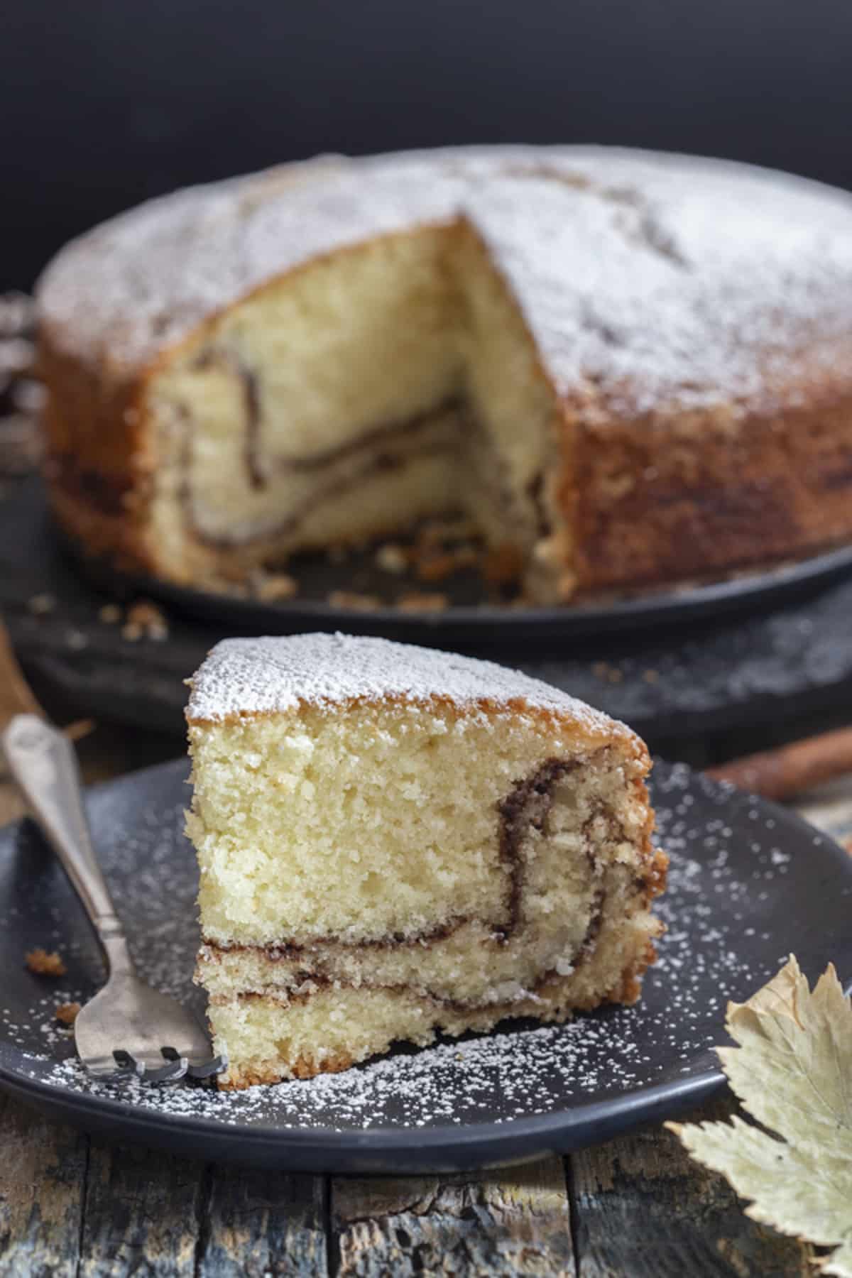 Cake on a cake stand with a slice on a black plate.