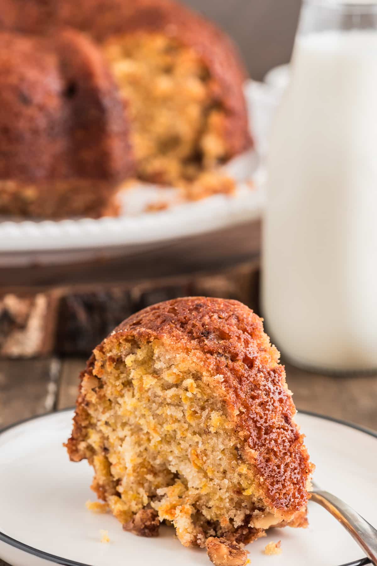 Carrot cake on a cake stand with a slice on a white plate.