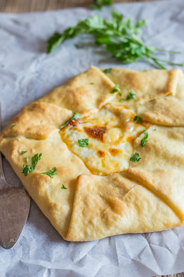 Rustic pie on parchment paper with fresh parsley & a silver server.