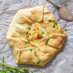 Rustic pie on parchment paper with fresh parsley & a silver server.