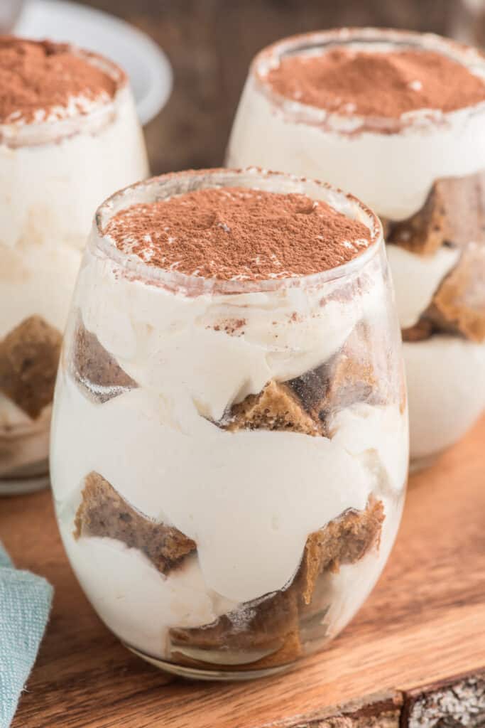 Three tiramisu parfaits in glasses on a wooden board.