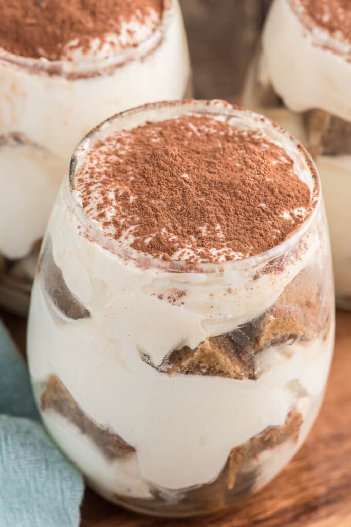 Three tiramisu parfaits in glasses on a wooden board.