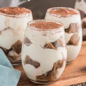 Three tiramisu parfaits in glasses on a wooden board.