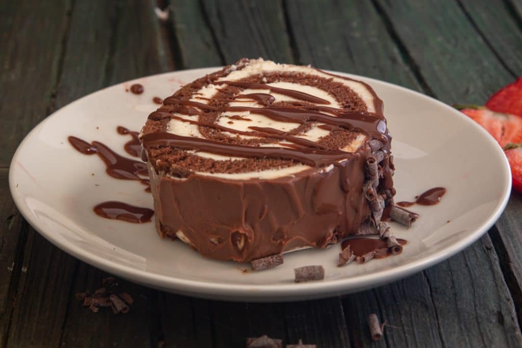 A slice of cake on a white plate drizzled with chocolate.