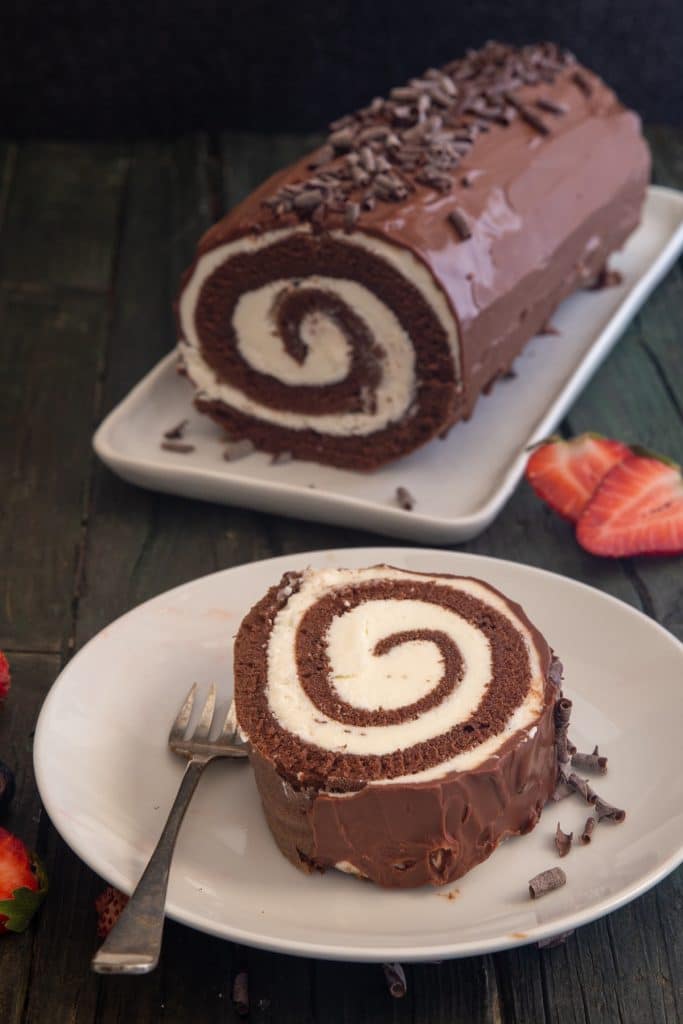 Roll cake on a white place with a slice cut on a white plate with a fork.