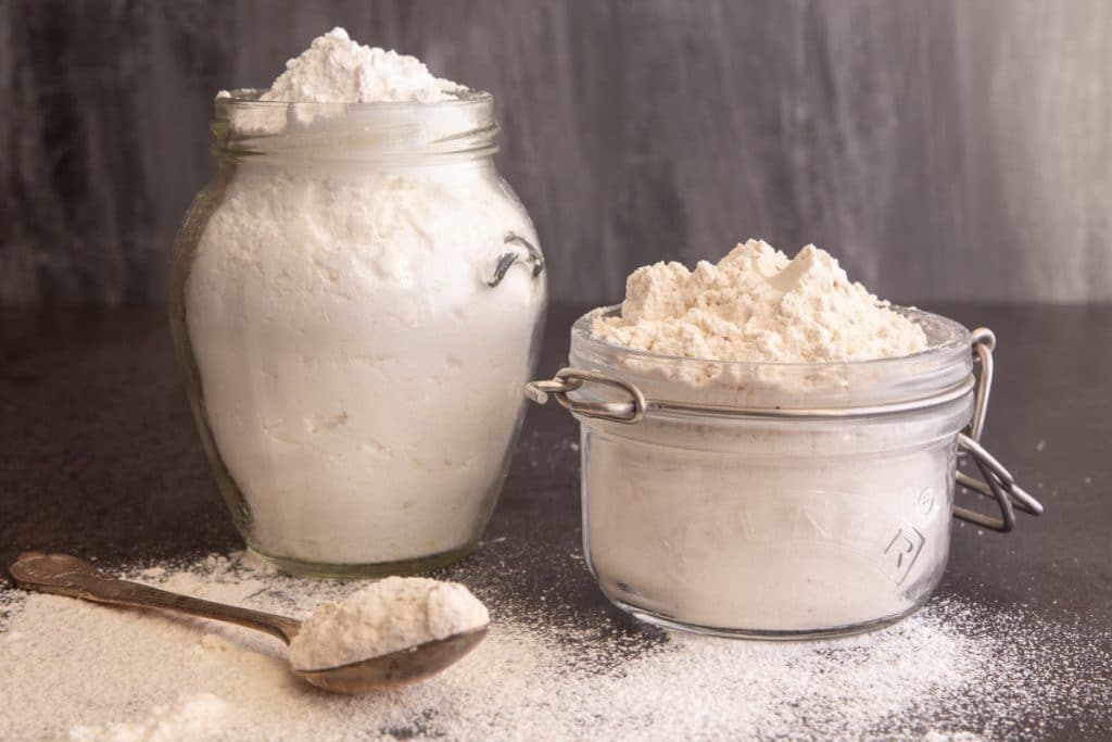 Brown and white powdered sugar in glass jars with some on a spoon.