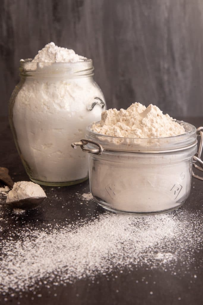 Brown and white powdered sugar in glass jars with some on a spoon.