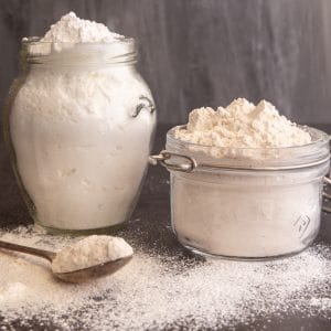 Brown and white powdered sugar in glass jars with some on a spoon.