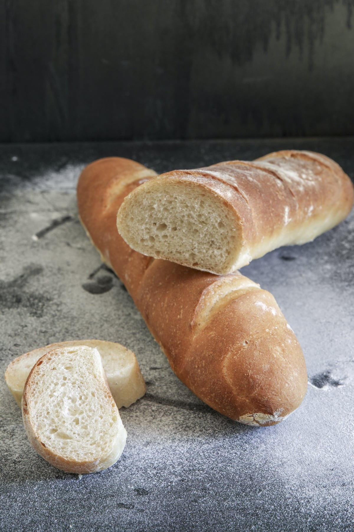 Two baguettes with two pieces on a floured board.