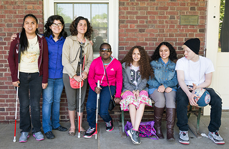 Group of teenagers, some with white canes standing against a brick wall. 