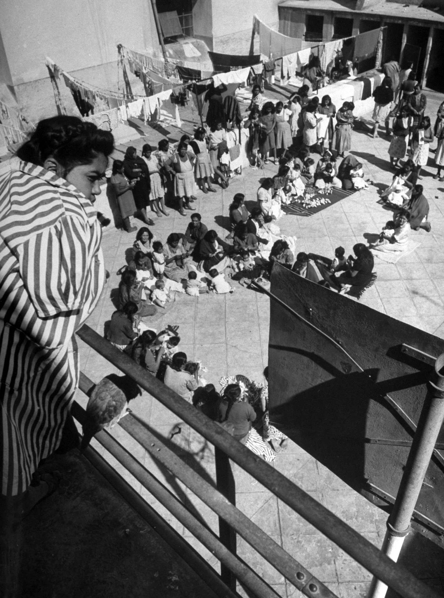 Prisoners relax with small children on a laundry-decked court. Prison stripes are not required and few of the women wear them.