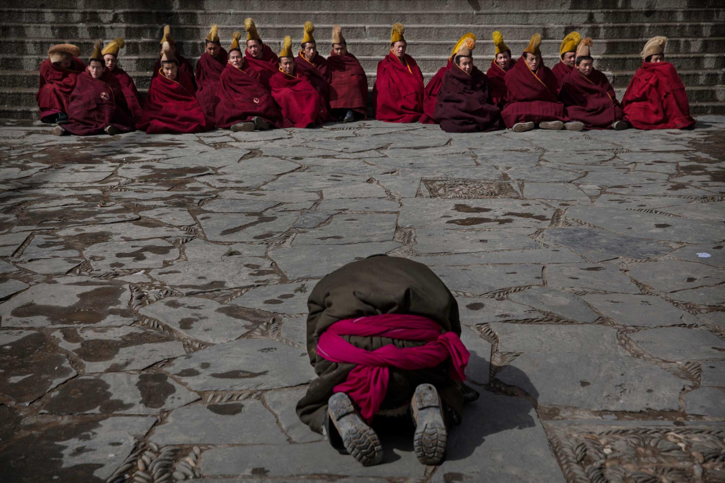 A Tibetan Buddhist man prays towards monks as they sit outside the main temple during Monlam or the Great Prayer ritualsat the Labrang Monastery, Xiahe County, Amdo, Tibetan Autonomous Prefecture, Gansu Province, China, March 5, 2015.