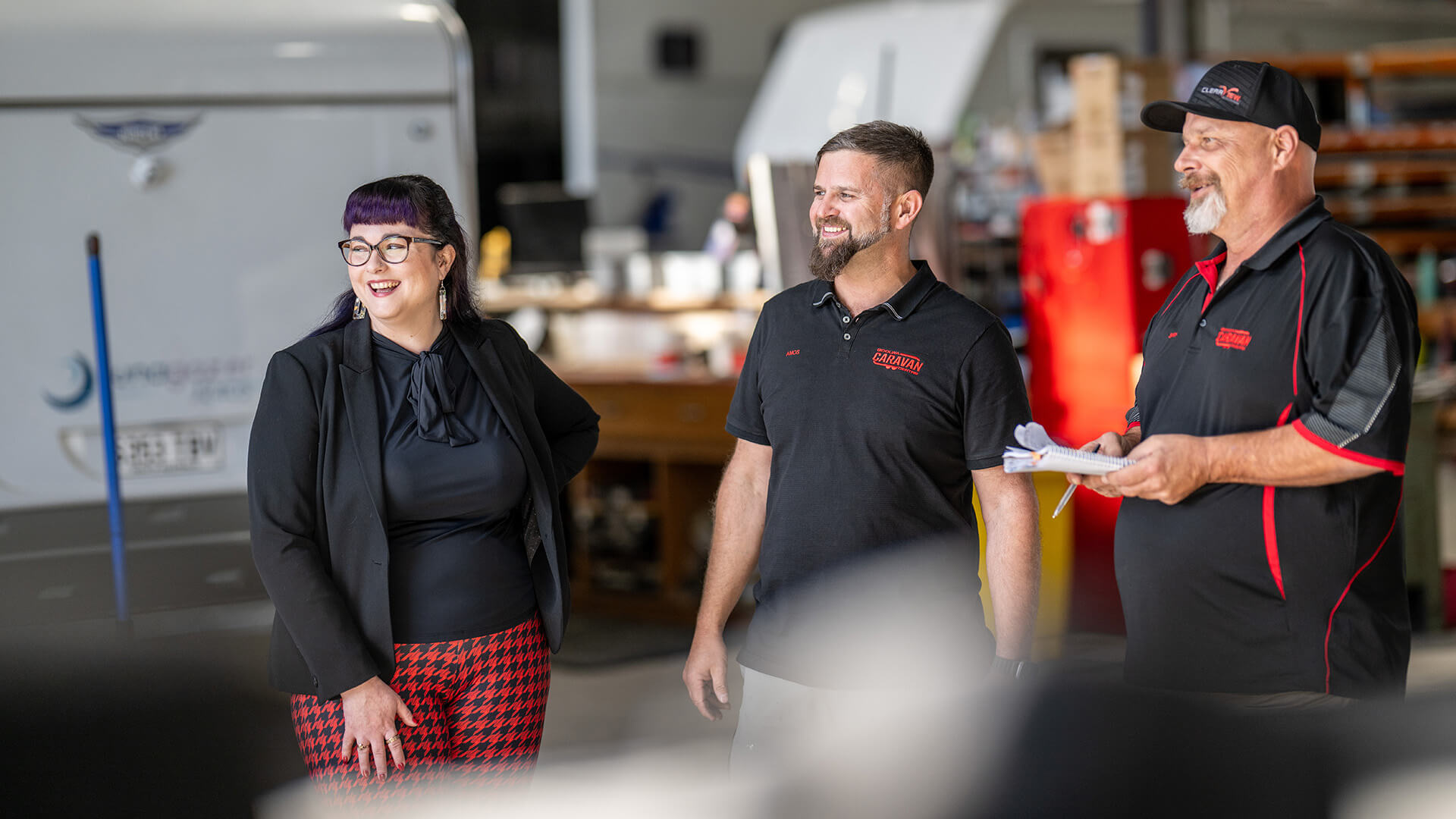 A woman and two men smile in conversation in a workshop