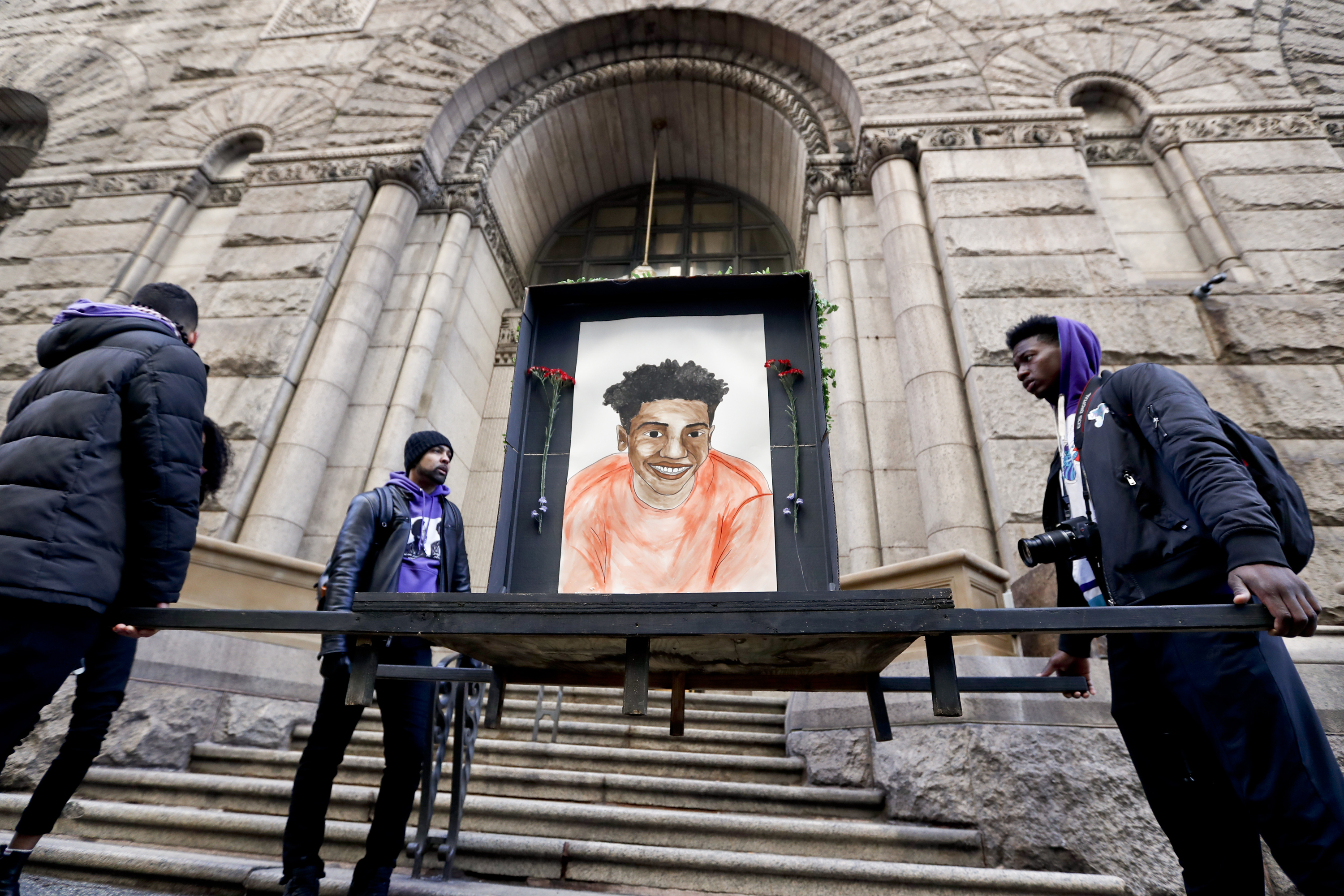 Farooq Al-Said, left, Jasiri X, center, and Jarrion Manning, right, hold a memorial display with a drawing of Antwon Rose II in front of the court house on the first day of the trial for Michael Rosfeld, a former police officer in East Pittsburgh, Pa., begins on Tuesday, March 19, 2019, in Pittsburgh. Rosfeld is charged with criminal homicide in the fatal shooting of Antwon Rose II as he fled during a traffic stop on June 19, 2018. (AP Photo/Keith Srakocic)