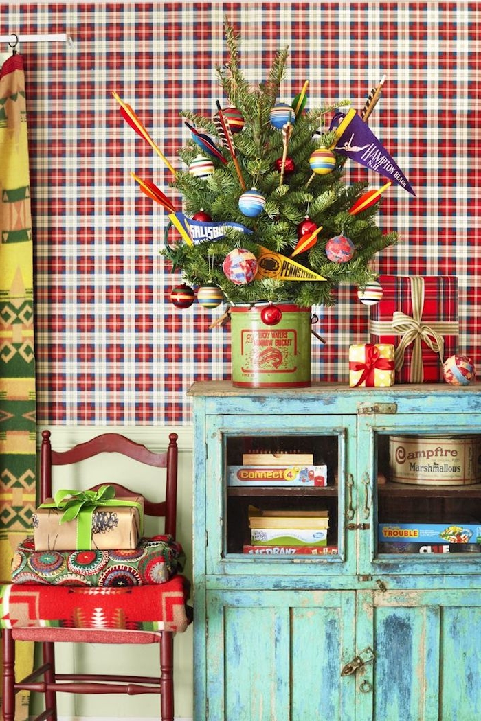 Kleiner Weihnachtsbaum in Eimer, geschmückt mit bunten Christbaumkugeln, vintage Möbel, karierte Tapete 