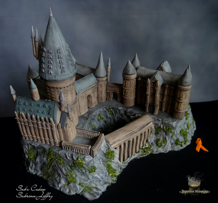 large cake in the shape of the whole hogwarts castle, happy birthday harry cake, made with fondant, placed on black surface