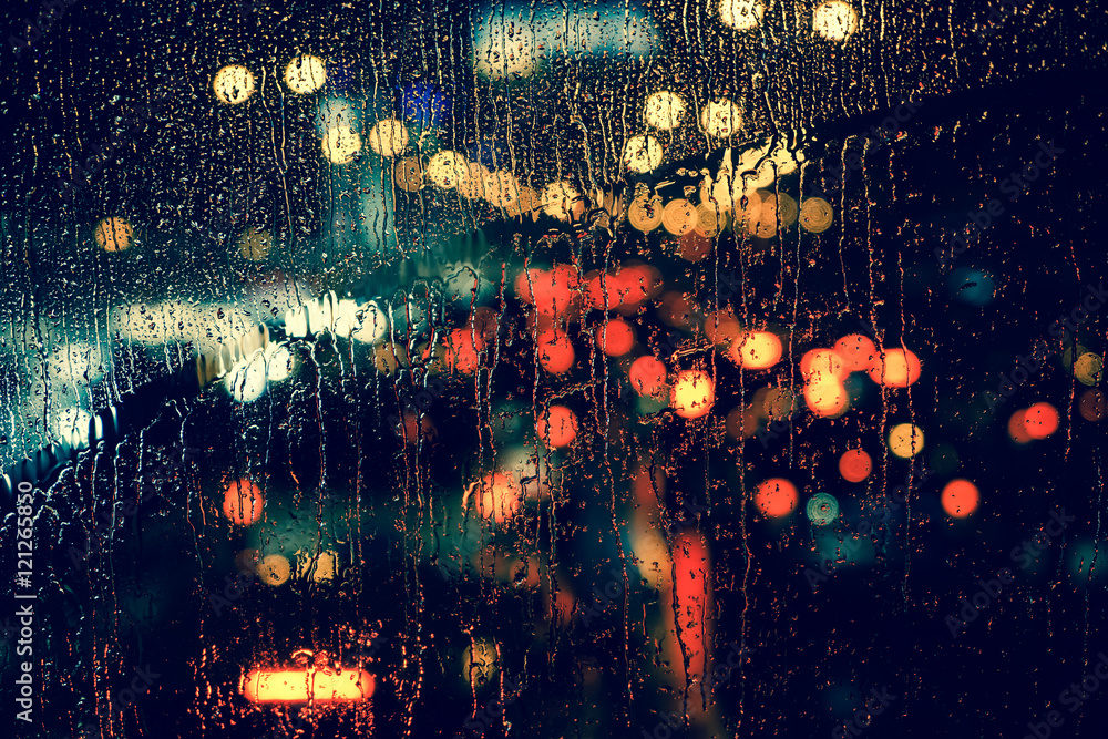 City view through a window on a rainy night,Rain drops on window with road light bokeh, City life in night in rainy season abstract background.