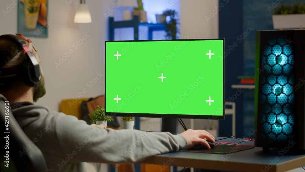 Pro gamer streaming video games with green screen mock-up display in gaming home studio. Player using RGB professional computer with chroma key isolated desktop playing shooter games wearing headset